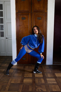 Woman in a blue outfit posing in a room with wooden floors and a large wooden door.